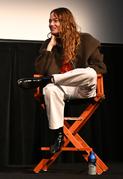 Emma Stone sitting in a director's chair in a brown jacket